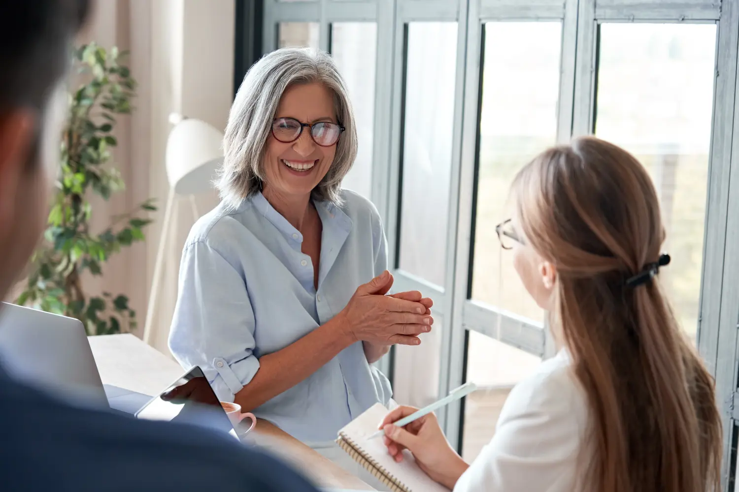 Forma, eine glückliche, reife Frau, die als Mentorin lachend junge Praktikanten bei einem professionellen Workshop im Gruppenbüro trainiert. 